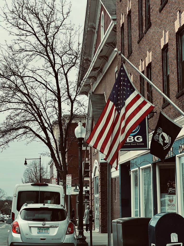 American flag waving on a street with cars and historical buildings.